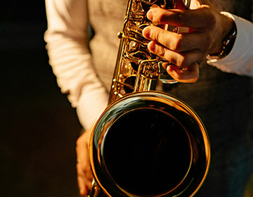 A saxophone player fingers keys against a black background
