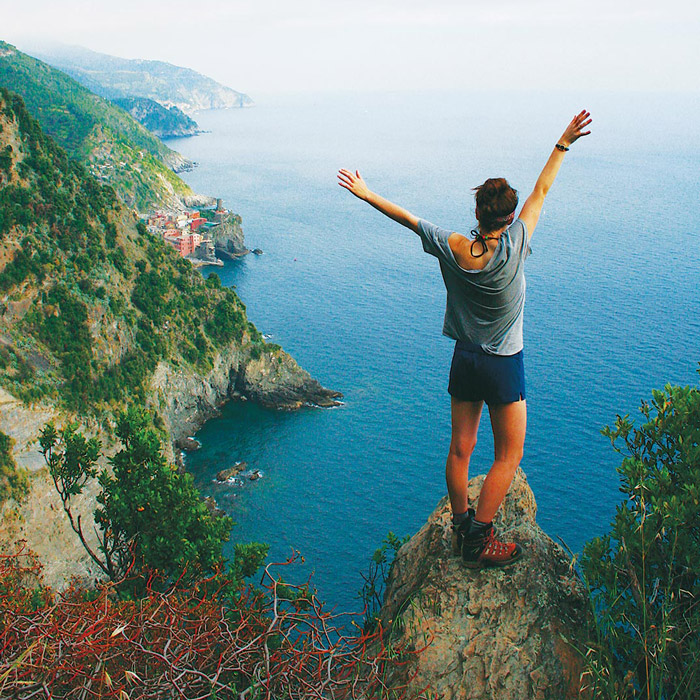 International student with arms raised overlooking scenic cliff