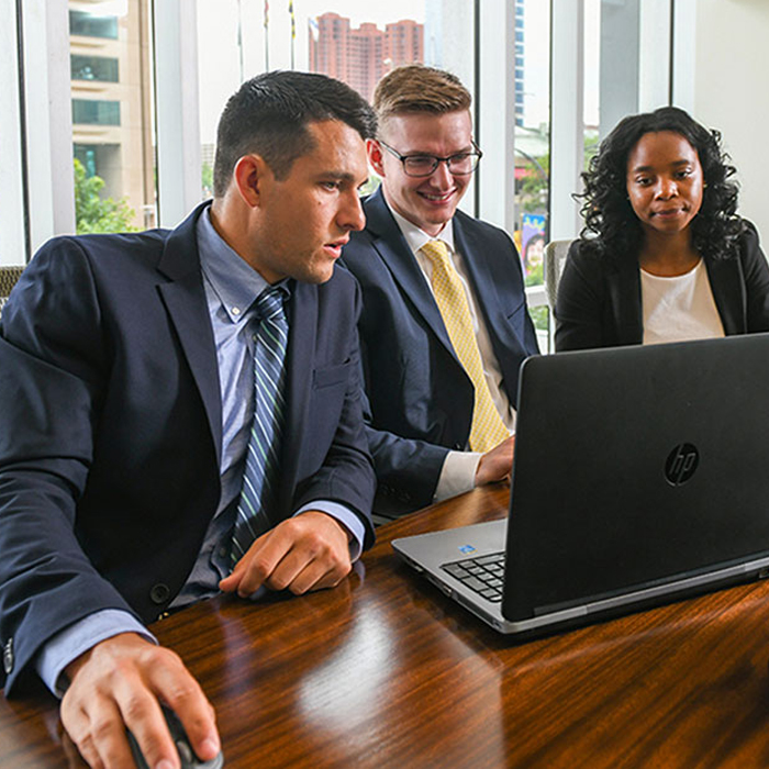 three business leaders in office looking at laptop