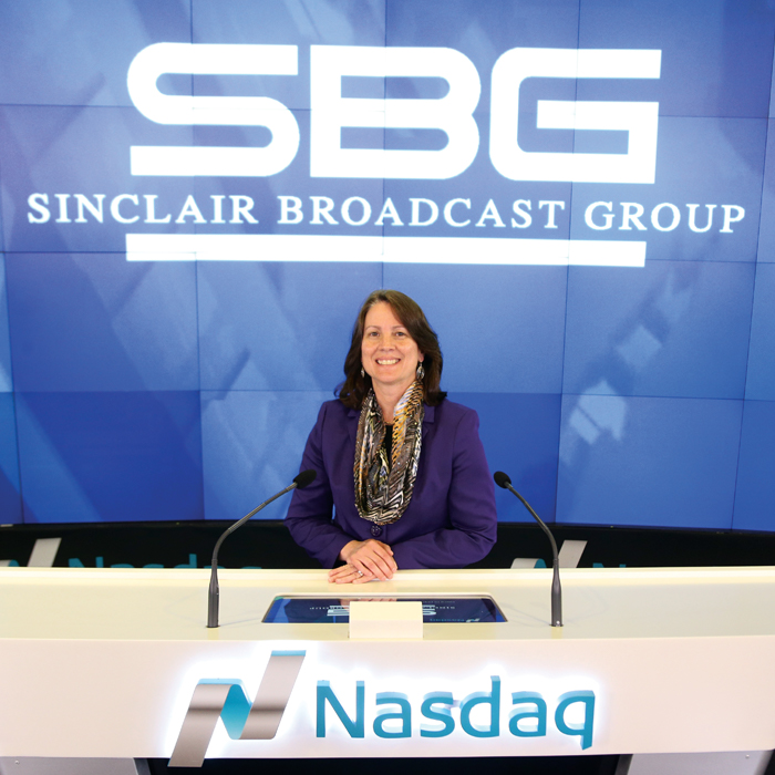 Lucy Motsay Rutishauser sitting in front of a sign that reads NASDAQ and Sinclair Broadcasting Group