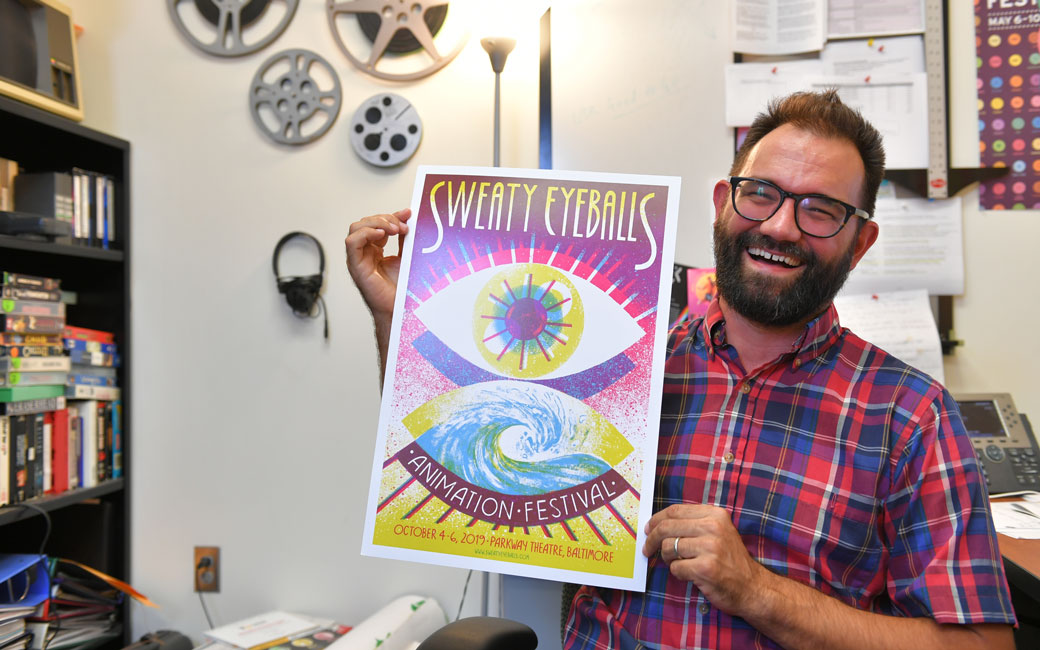 Professor Phil Davis holds up a poster for the Sweaty Eyeballs Animation Festival