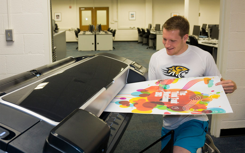 Student examining a poster as it prints in the SCS Lab in Cook Library