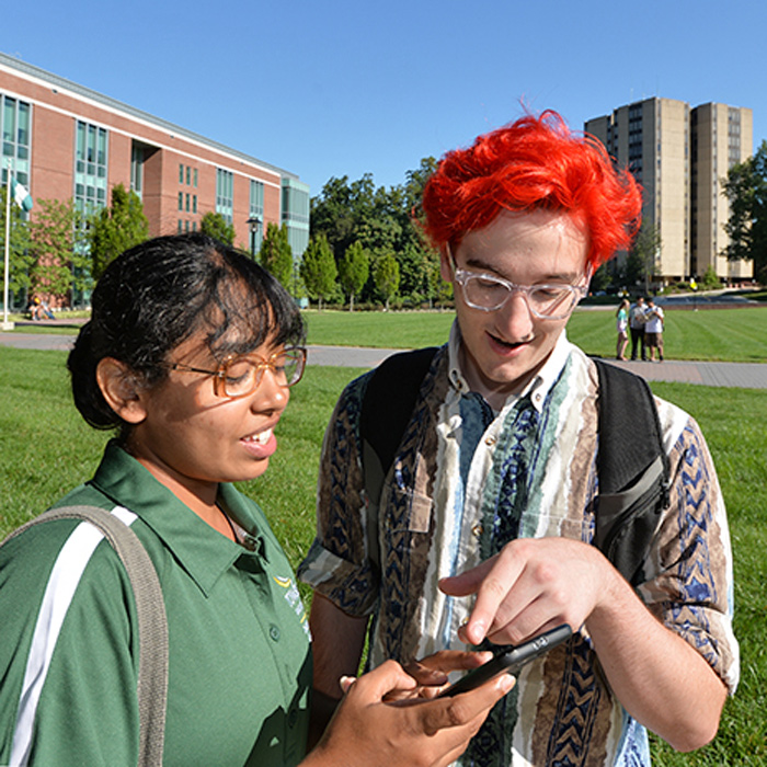 two students looking at a smartphone with the Residence Tower in the background
