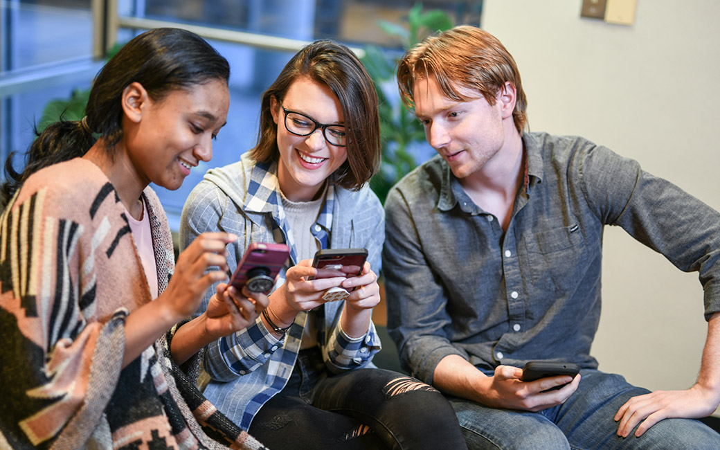 three students on campus looking at their phones