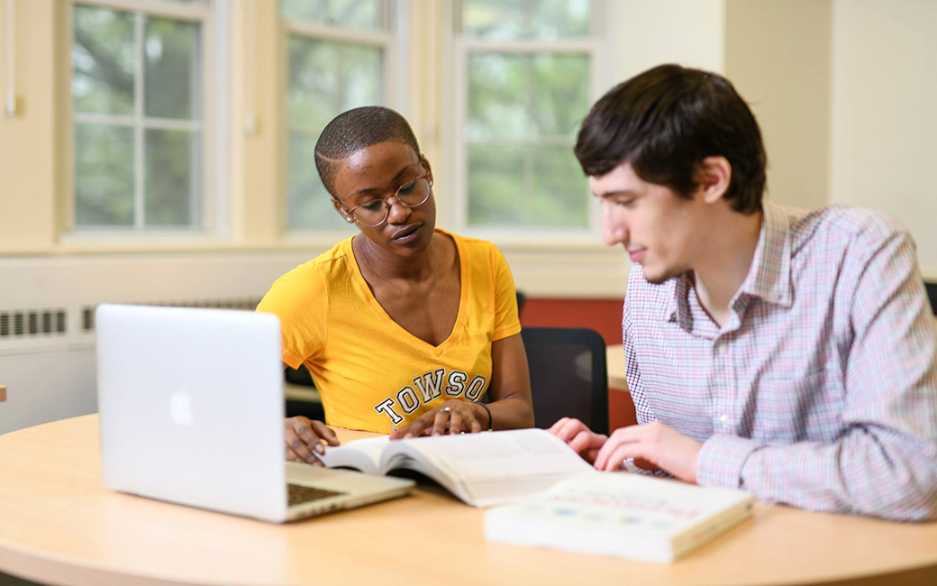 Two Towson Univeristy students studrying with a laptop and books in one of the classrooms 