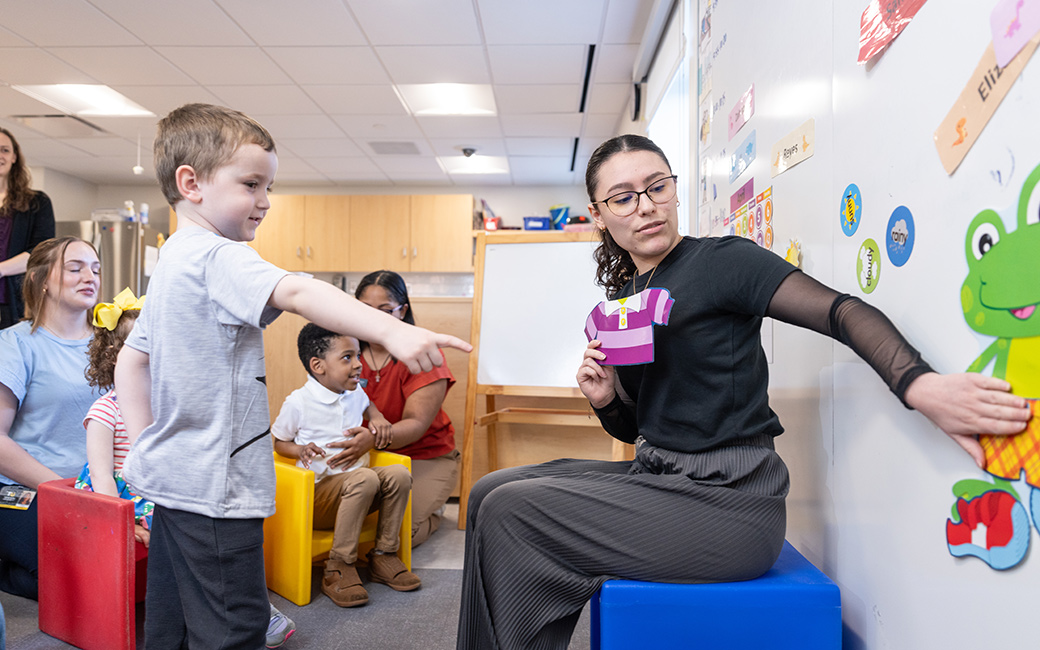 student helping child dress cartoon frog