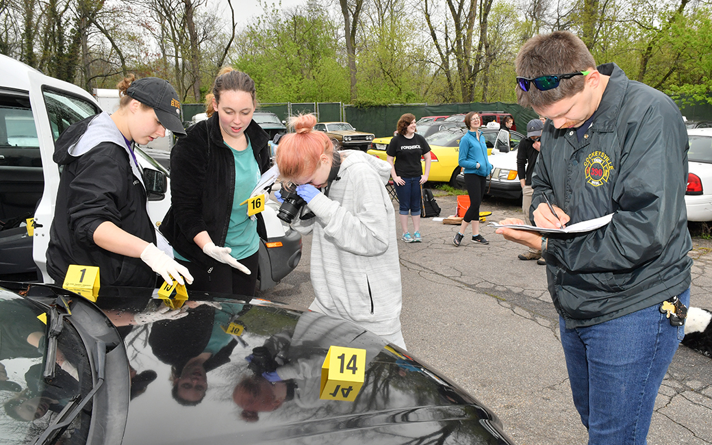 students investigate the hood of a car with labeled sections, as part of their training in crime scene investigations