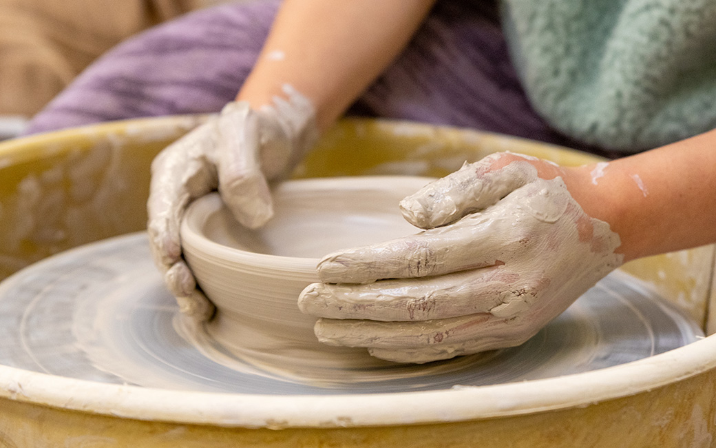hands throwing a pot on a wheel in ceramics class
