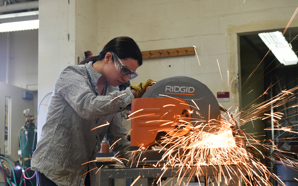 female sculpture student using saw, sparks flying