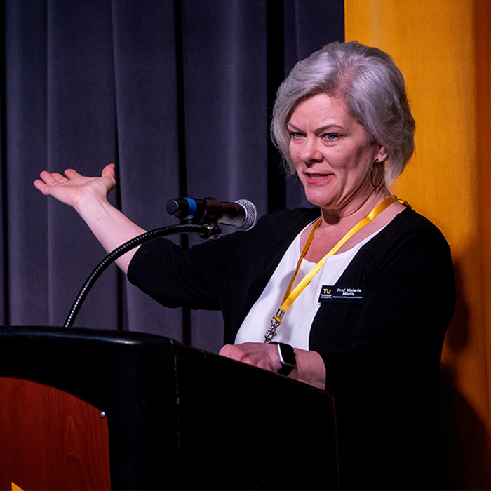 A faculty member speaking on stage at a podium