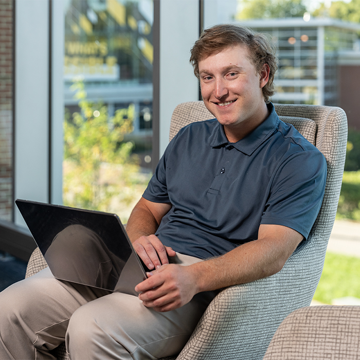 A student in the University Union smiling at the camera while he works on his laptop