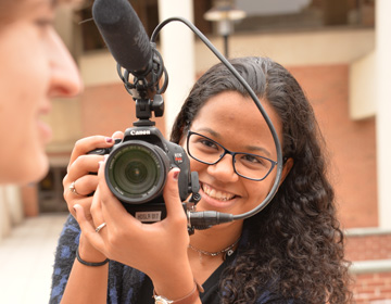 A smiling students holds up a video camera