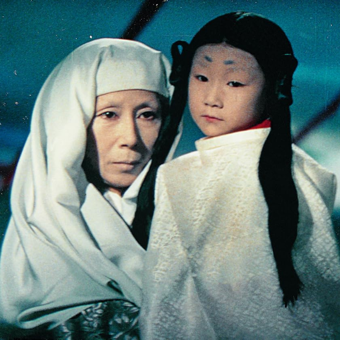 Kwaidan (怪談) A color film still from the 1964 Japanese anthology horror film Kwaidan (directed by Masaki Kobayashi), depicting a woman and a young child.On the left, an older woman looks onward with a solemn expression, wearing a draped white head covering that frames her face. To her right, a young child stands looking directly at the camera, wearing traditional white clothing with a red collar. The child features distinct historical makeup, including high, painted-on eyebrows, and long black hair styled into two prominent side braids.