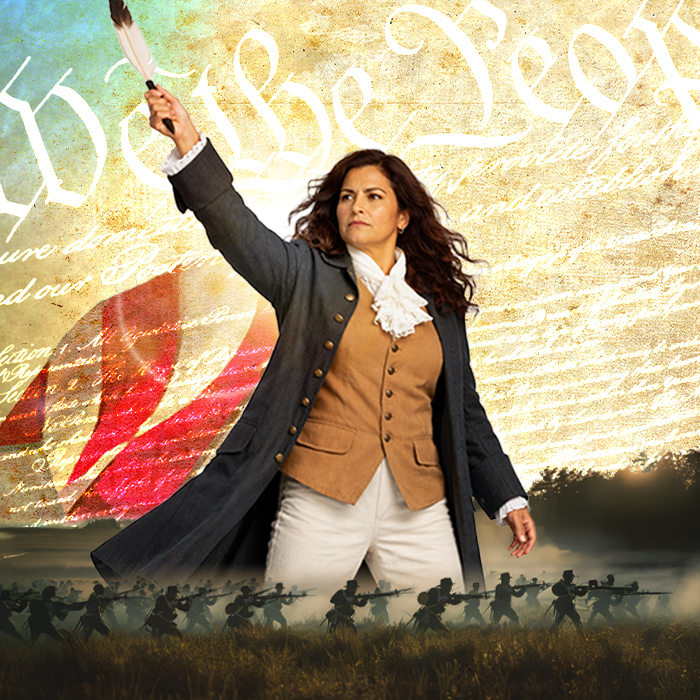 A woman in 1770s mens coat, waistcoat, and britches holds a quill pen up like a majestic sword