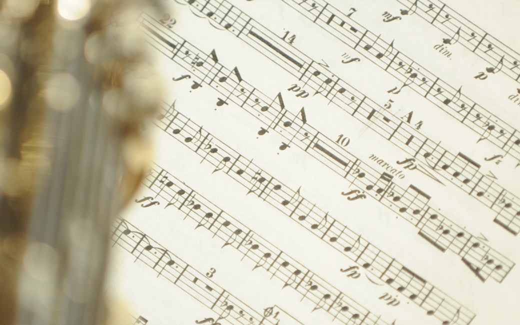 A close up on quick-tempo sheet music, with a brass instrument just off to the side