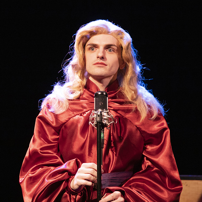 A scene from Lily, Arthur: A singer in a 1940s-style wig and fancy dress nervously stands at a microphone