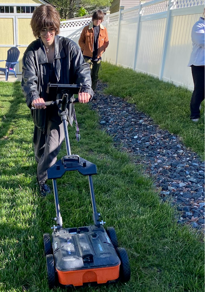student pushing a ground penetrating radar on the grass