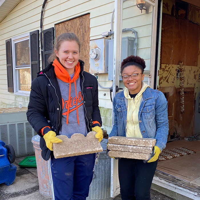 Two smiling students carrying bricks at a Habitat for Humanity site