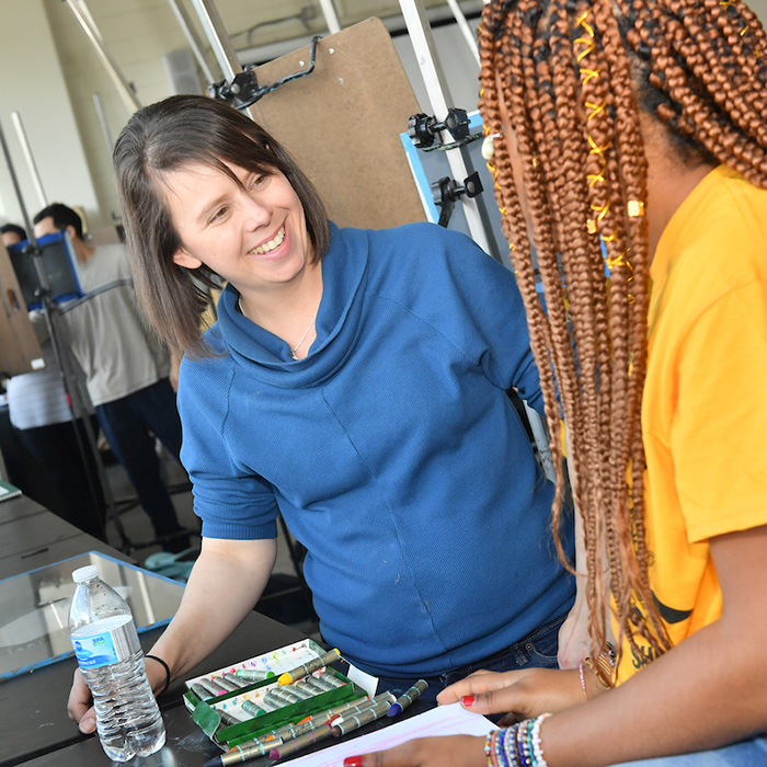 Female faculty member smiling and giving instruction to a student