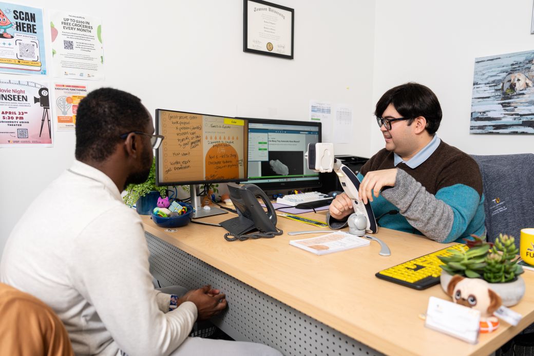 An ADS Specialist demostrating a physical document magnifier with a student inside an office.
