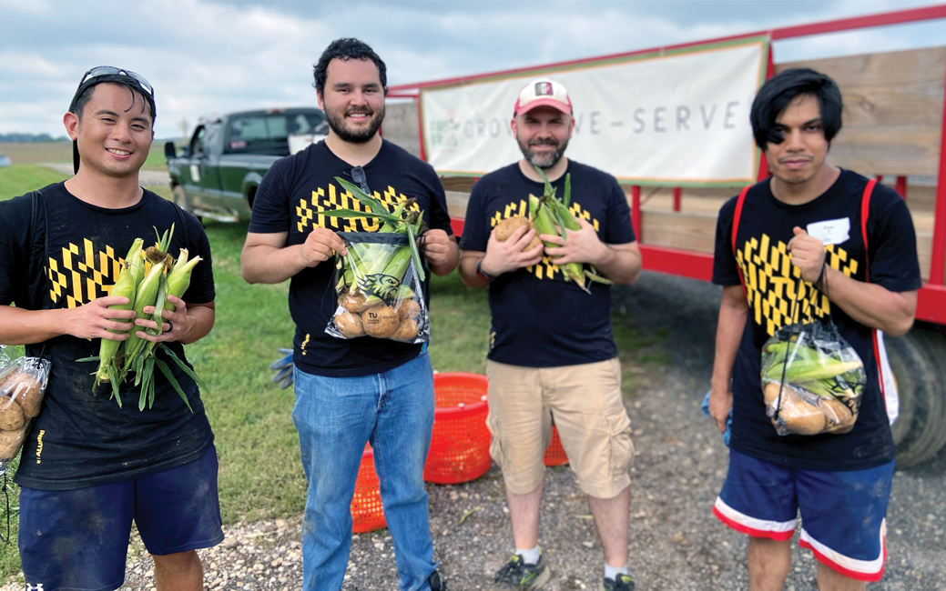 A group of people wearing black and gold t-shirts outside holding vegetables