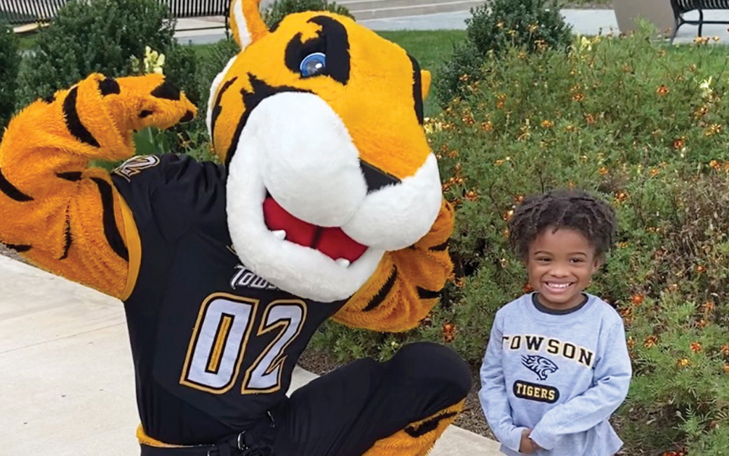 A small child smiling next to the mascot Doc the Tiger, who is flexing his arms