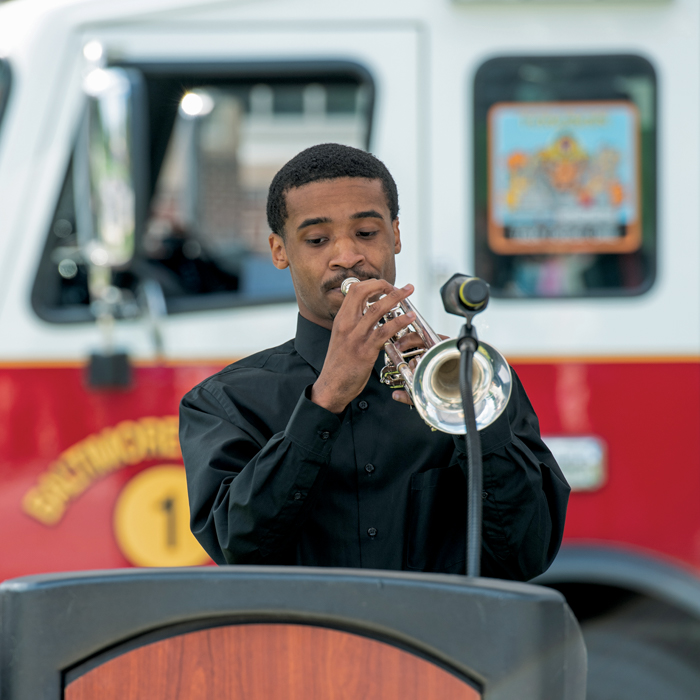 Person playing trumpet at a podium in front of a fire truck