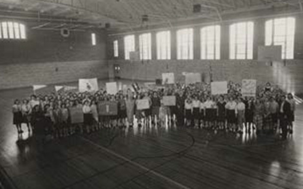 Black and white photo of a large number of people standing in a gymnasium