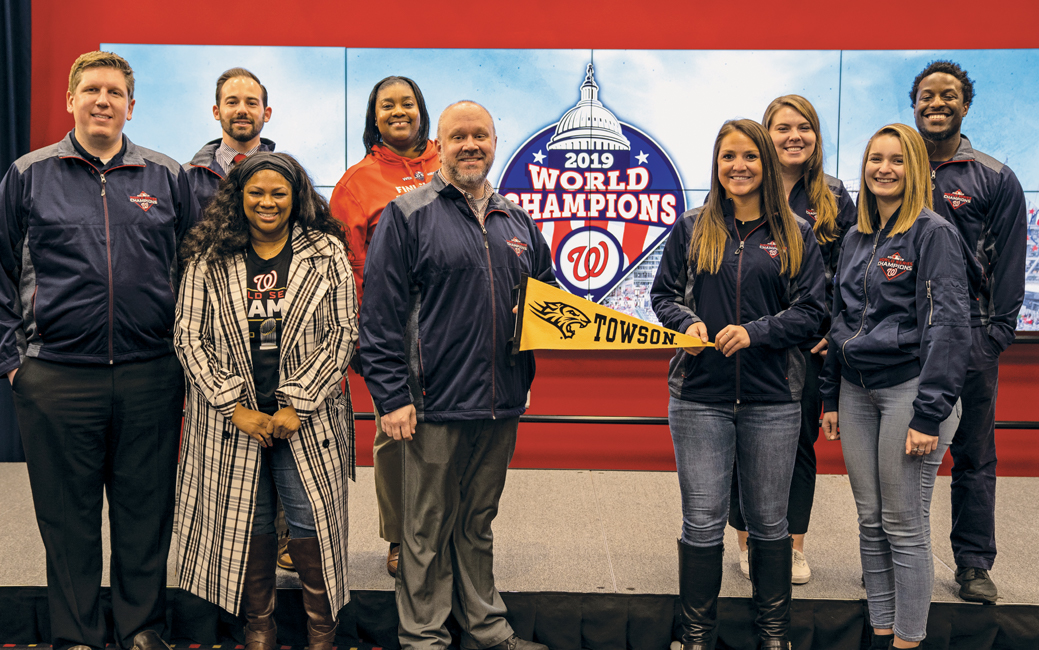 Alums holding a Towson pennat in front of a Nationals World Series champions logo