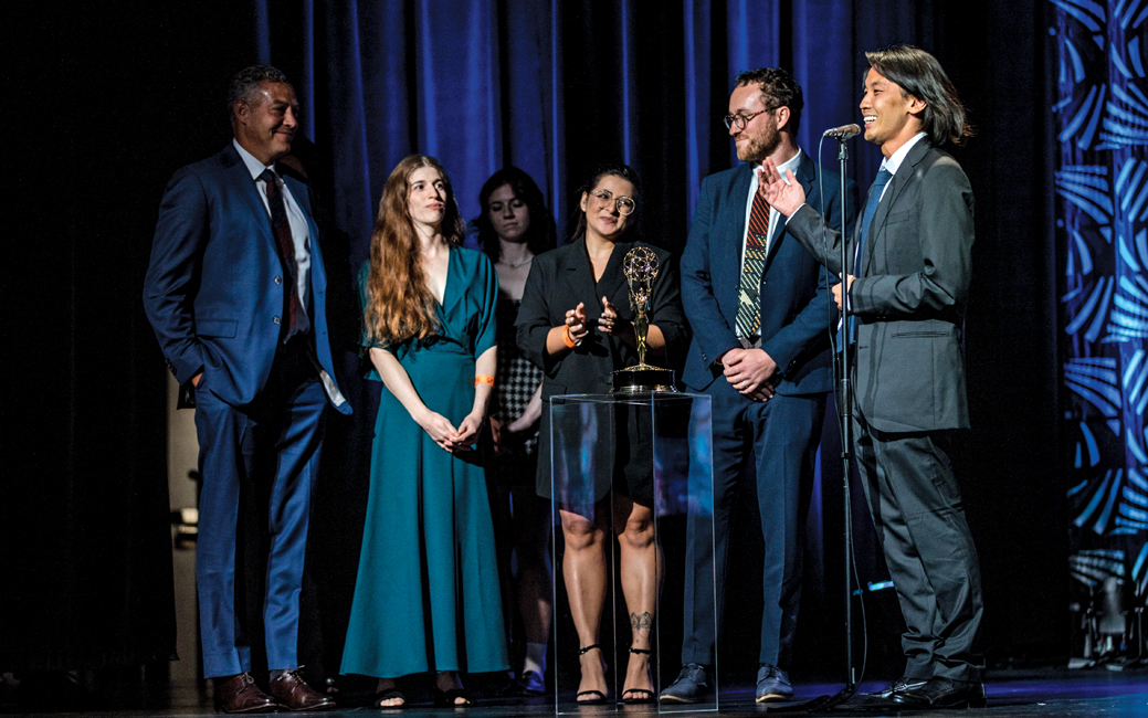 group of people standing on a stage, one is holding an award