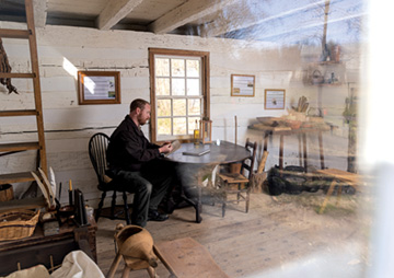 Jonathan Wood sitting in an historical interpretation of Benjamin Banneker's cabin