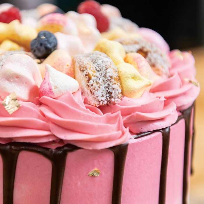 close up of a pink cake with chocolate drizzle that is topped with meringues