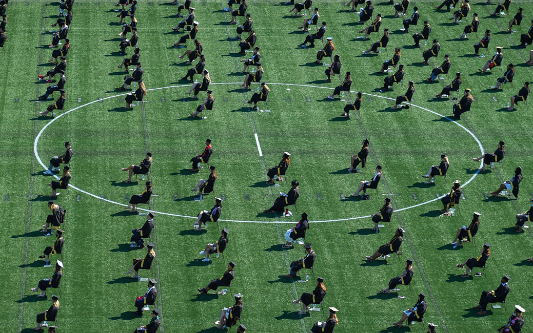 Socially distanced graduates sit in chairs on a football field