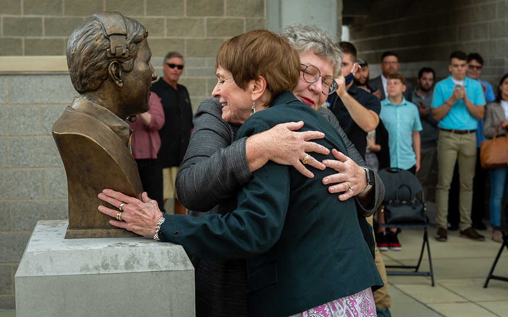 People embrace next to bust statue