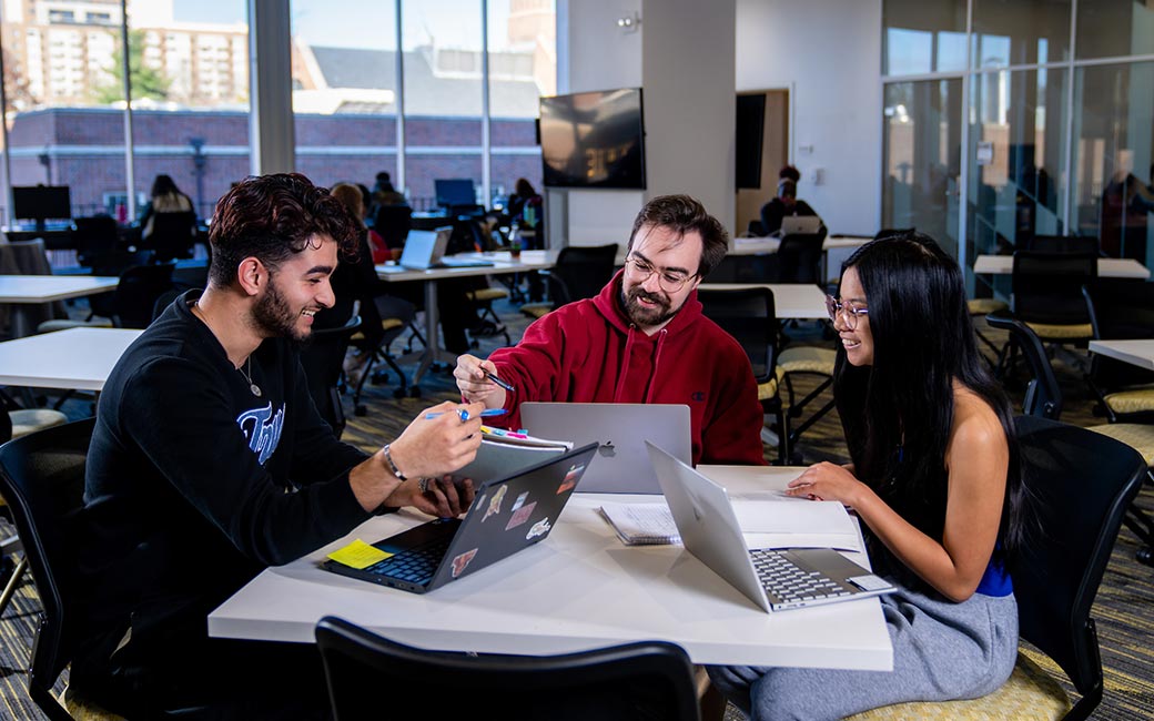 Students sit at table in open study area