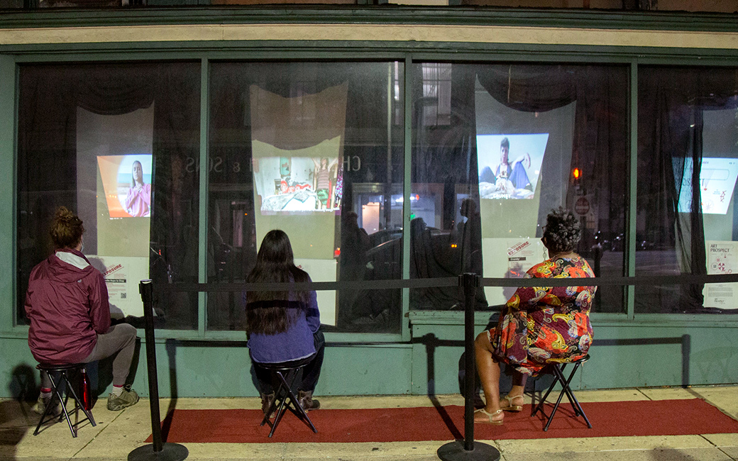 People sit on stools outside a window display at night