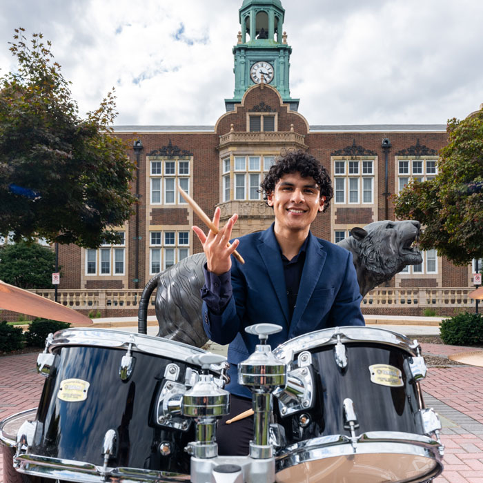 Brandon Reyes spinning a drum stick while sitting in front of Stephens Hall 