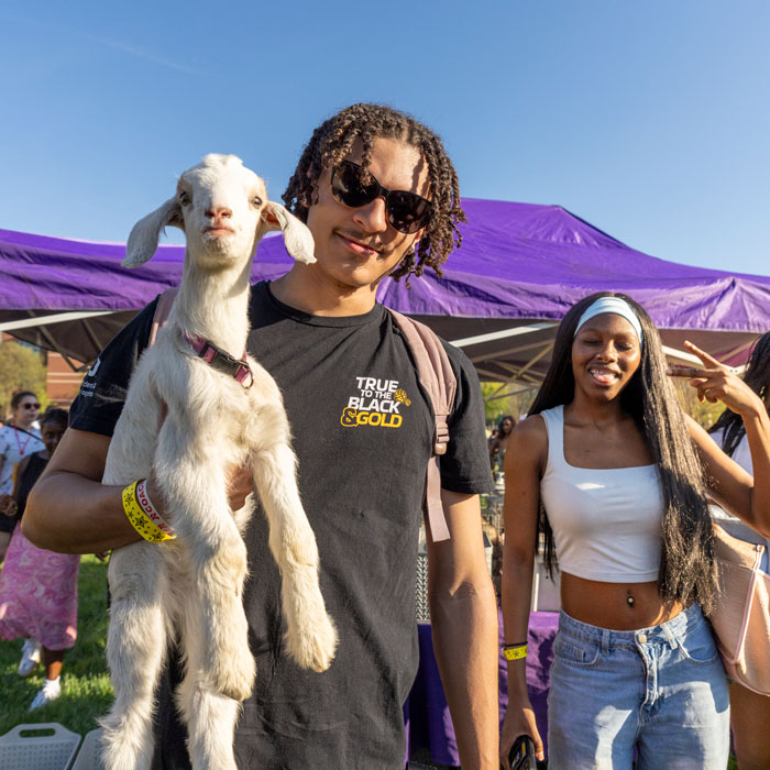 Student holds a goat from the petting zoo at CAB's Tropical Fever event