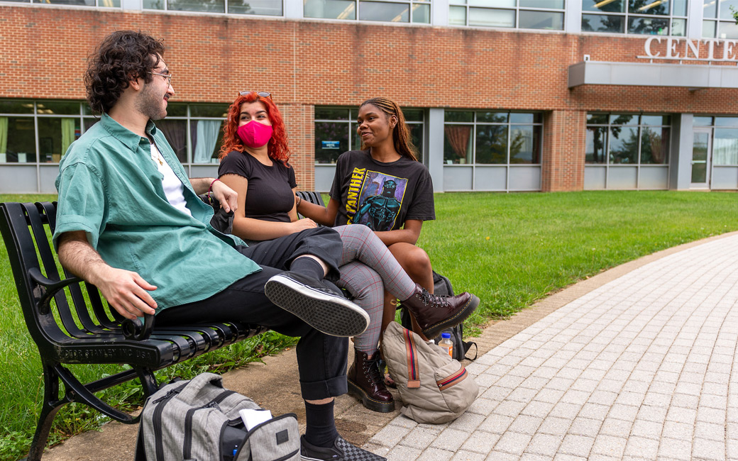 Three students sit on a bench outside the Center for the Arts