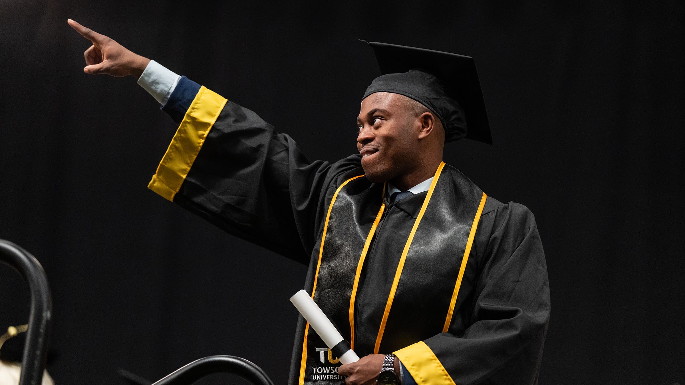 Student in commencement regalia, pointing triumphantly 