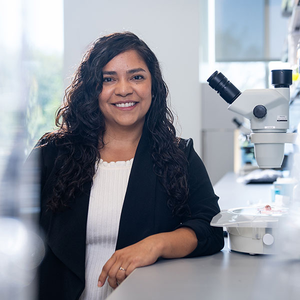 Woman leans on lab station next to microscope
