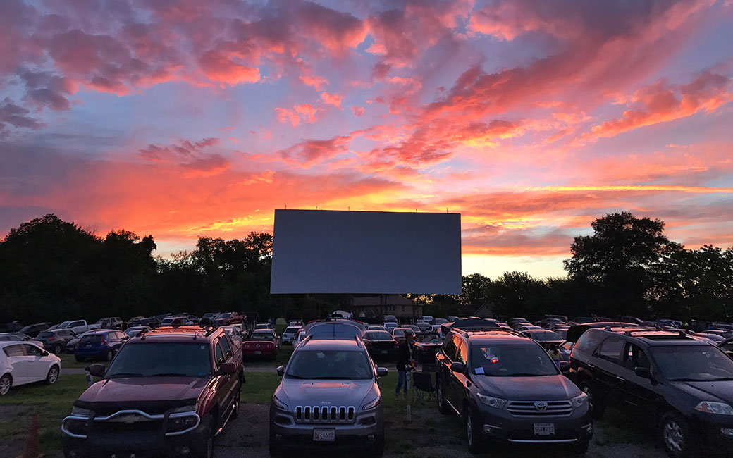 Drive-in movie screen with parked cars at sunset