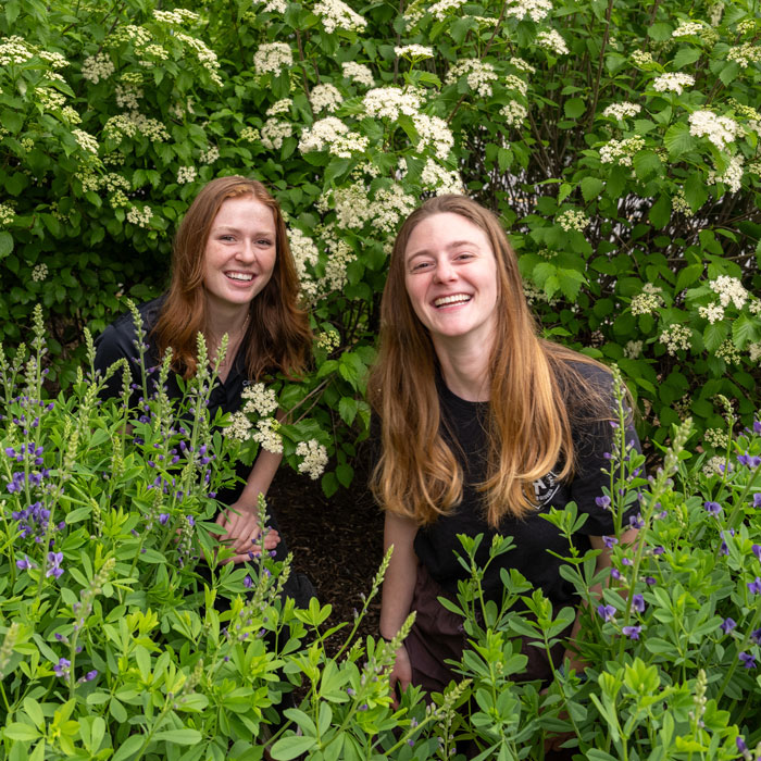 Kennedy Krohn and Zoe Huff pose for a picture in some plant life 