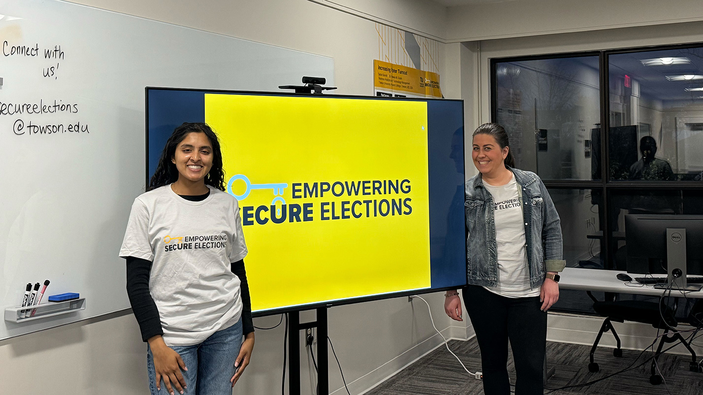 two people standing next to "Empowering Secure Elections" sign