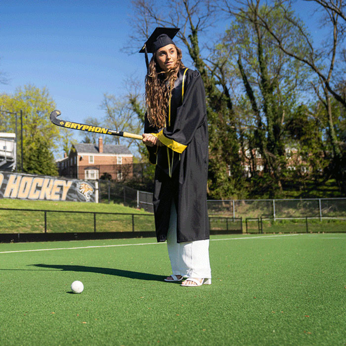 GIF of student in cap and gown hitting field hockey ball