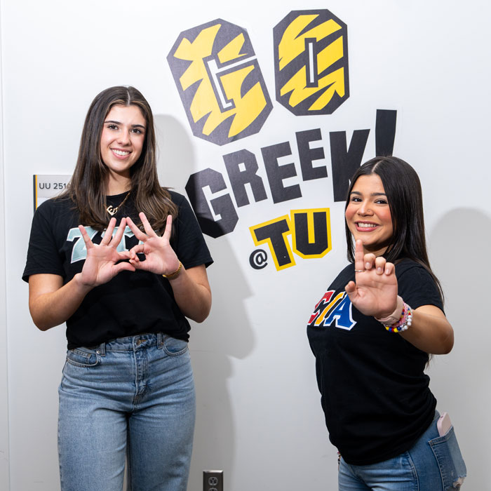 Two sorority members stand next to the Go Greek TU sign.