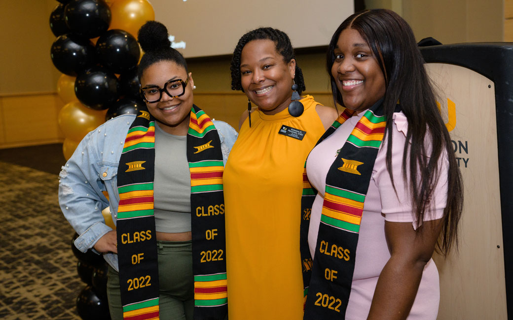 Three people pose at celebration with two wearing kente stoles