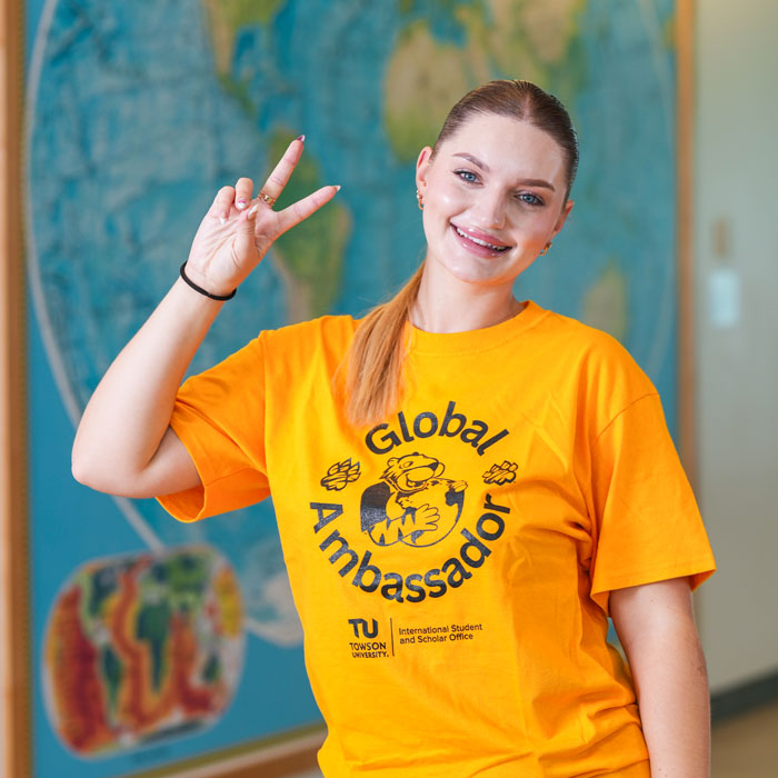 Sofiia holds up a peace sign while standing in front of one of the world maps located in the Liberal Arts Building