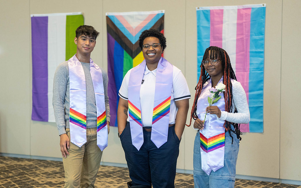 Three people wearing stoles in front of pride flags