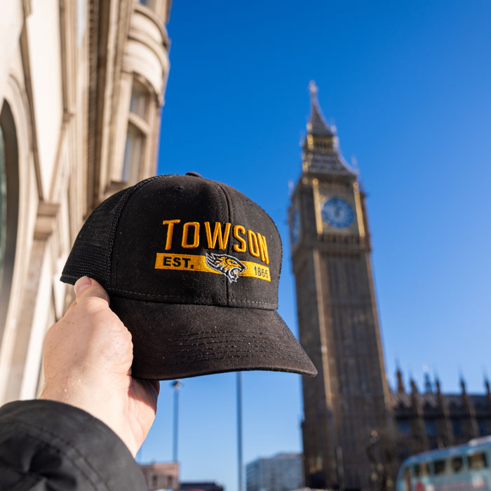Towson University baseball cap is held in the air with Big Ben in the background